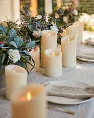 Outdoor dining table decorated with faux candles, artificial spring garland, taupe tablecloth, plates, and napkins