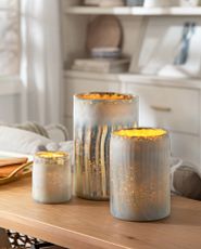 Set of three mercury glass hurricanes with a creamy white finish on top of a console table in the living room