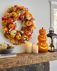 Fall wreath on a mantel decorated with candles, lanterns, and Halloween pumpkin decorations
